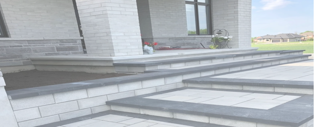 Wide view of light slab steps with dark caps running along the front of a brick house to a paved landing