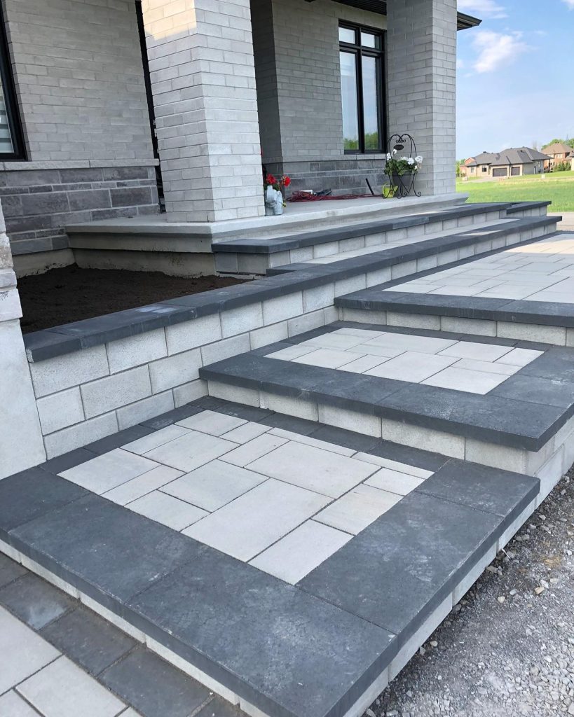 Wide light slab steps with dark treads and caps leading up to the covered entrance of a pale brick house