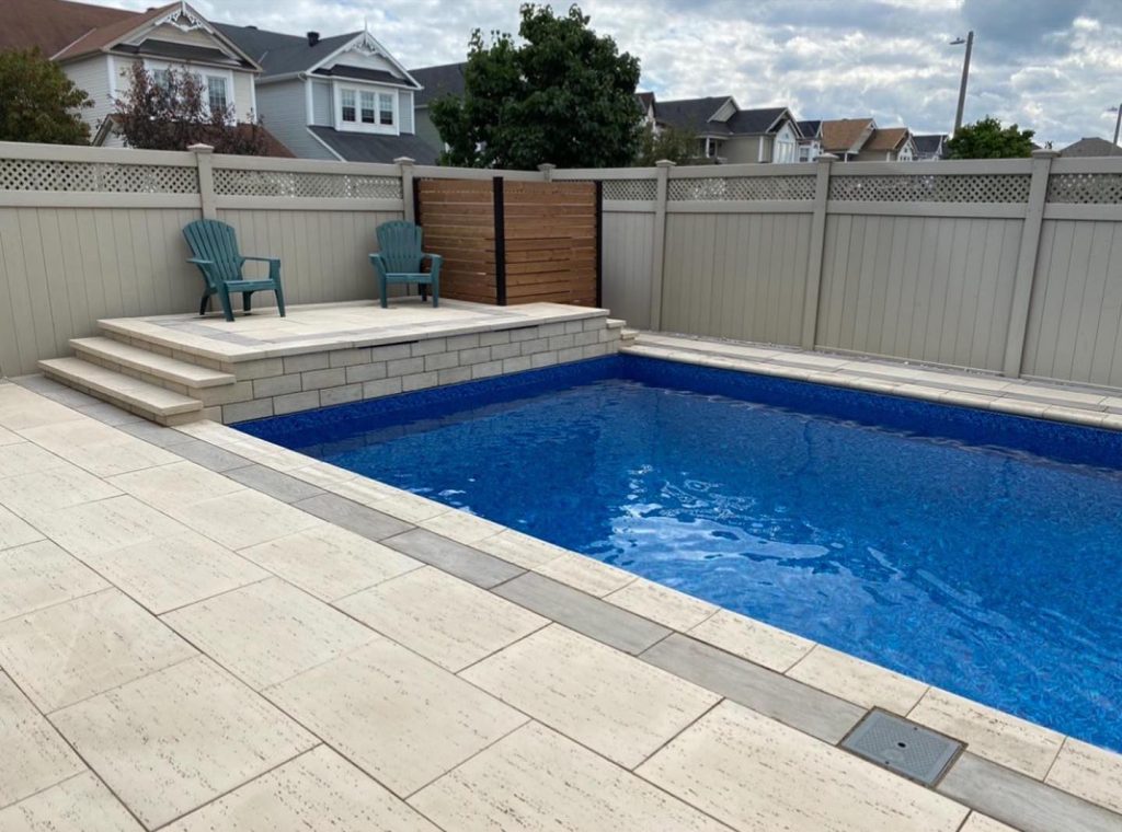 Rectangular pool surrounded by pale paving, with a raised seating deck, block wall and wood privacy screen