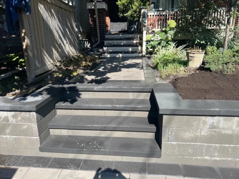 Paver steps set into a block retaining wall, leading to a walkway between a wood fence and a planted bed