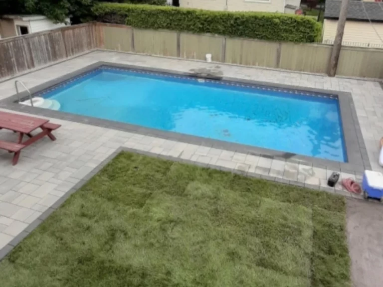 Rectangular pool with pale paving and new sod in a fenced backyard
