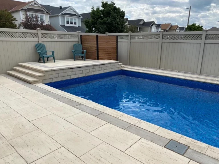 Rectangular pool surrounded by pale paving, with a raised seating deck, block wall and wood privacy screen