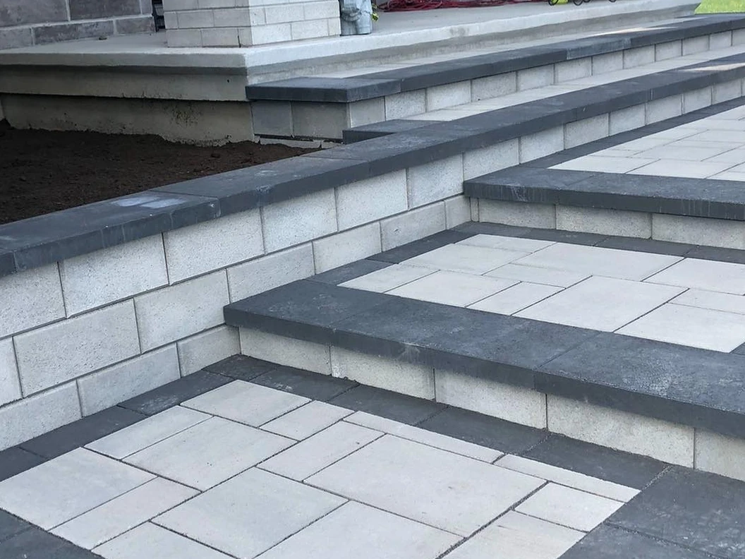 Wide light slab steps with dark treads and caps leading up to the covered entrance of a pale brick house