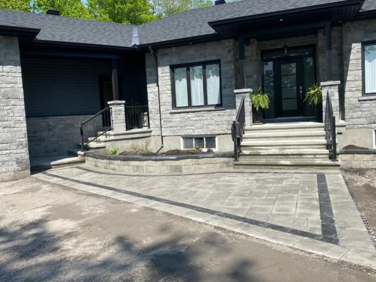 Front entrance of a stone-clad bungalow with wide paver steps and a light interlock walkway running to the driveway